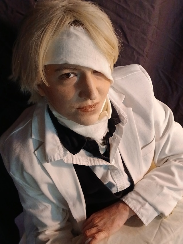 Image: Photo of the site owner dressed as Rufus Shinra from the movie Final Fantasy VII Advent Children, sitting with a small rectangular box covered by a white sheet