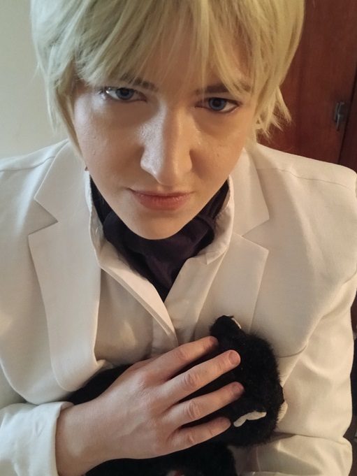 Image: Photo of the site owner dressed as Rufus Shinra from the game Final Fantasy 7 Before Crisis, facing the camera with a menacing expression and stroking a plush tuxedo cat