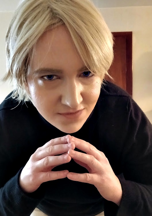 Image: Photo of the site owner dressed as Rufus Shinra from the game Final Fantasy 7 in a black turtleneck and blond wig, smirking at the viewer with tented fingers